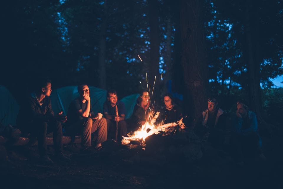 Grupo de personas reunidas alrededor de un fuego de noche