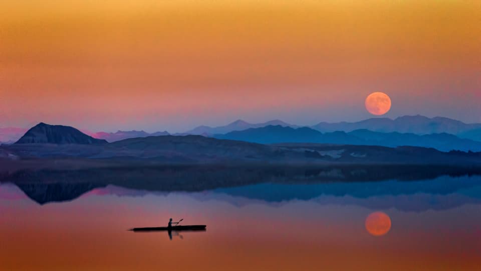 Kayak navegando un lago al atardecer con la luna