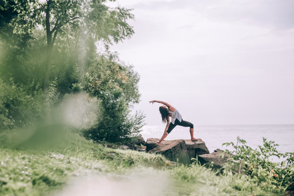 Mujer practicando yoga sobre una roca rodeada de vegetación
